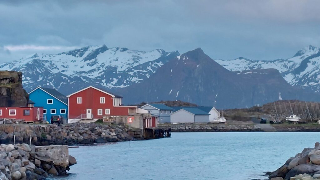 Vista al mar y la montanas con nieve en islas lofoten en noruega. se ve cabana de madera en el fondo.