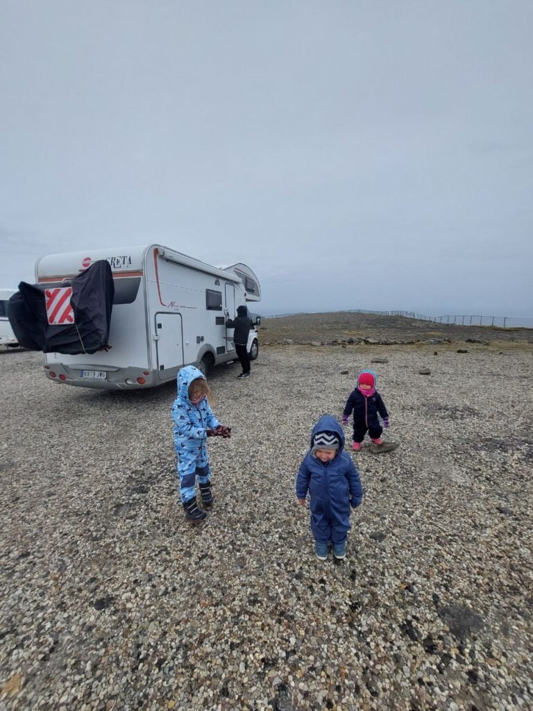 3 ninos enfrente de autocaravana en el parking