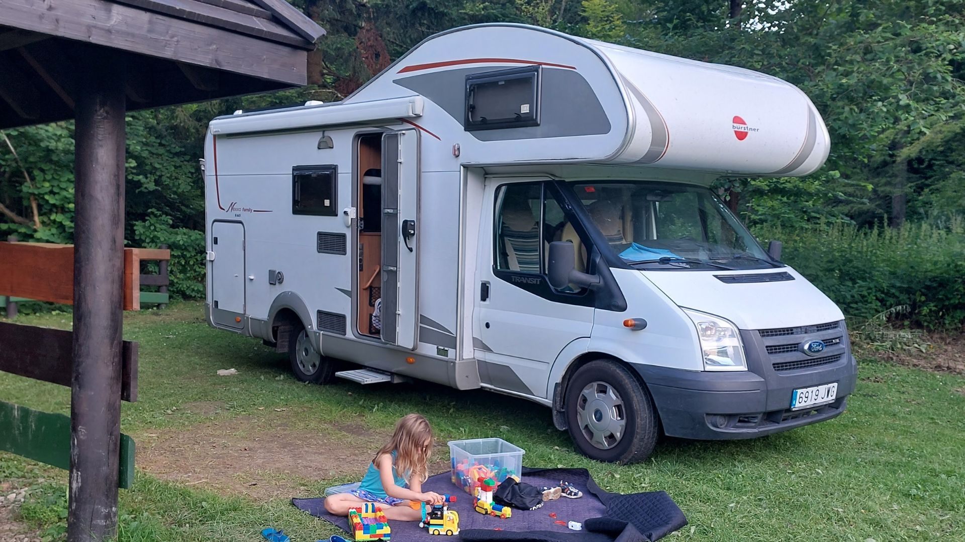 autocaravana capuchina aparcada en el bosque con la niña jugando lego enfrente de ella