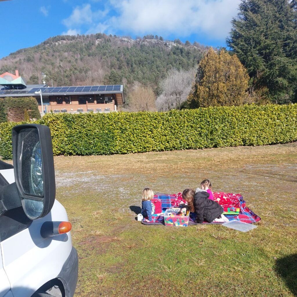 tres ninos juguando en el cesped, al lado de autocaravana en Camping Vall de Camprodon